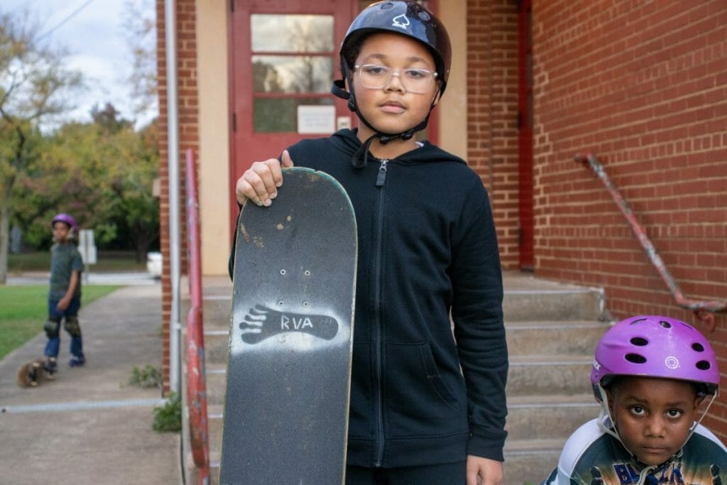 Young skateboarder holding skateboard featuring "RVA" stencil